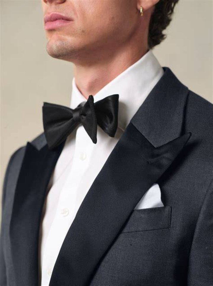 He is wearing a tuxedo, she is wearing a white wedding dress as they are holding hands.