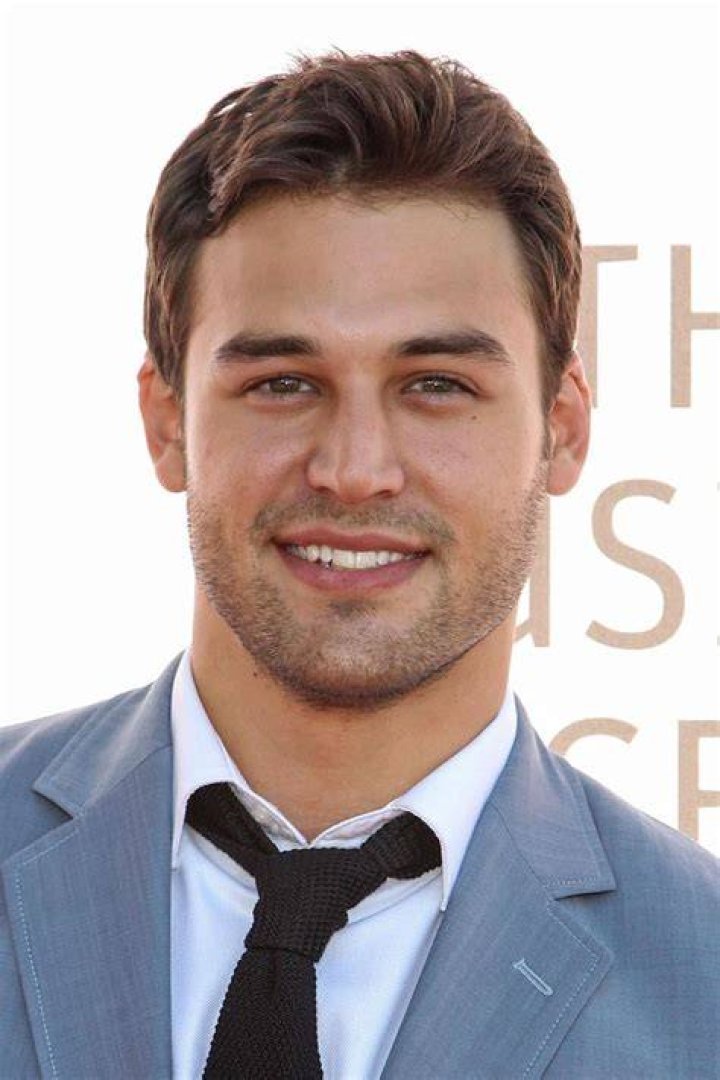 Ryan Guzman in shirt and jeans sitting on chair