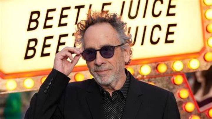 Tim Burton is wearing a black suit and a spec.